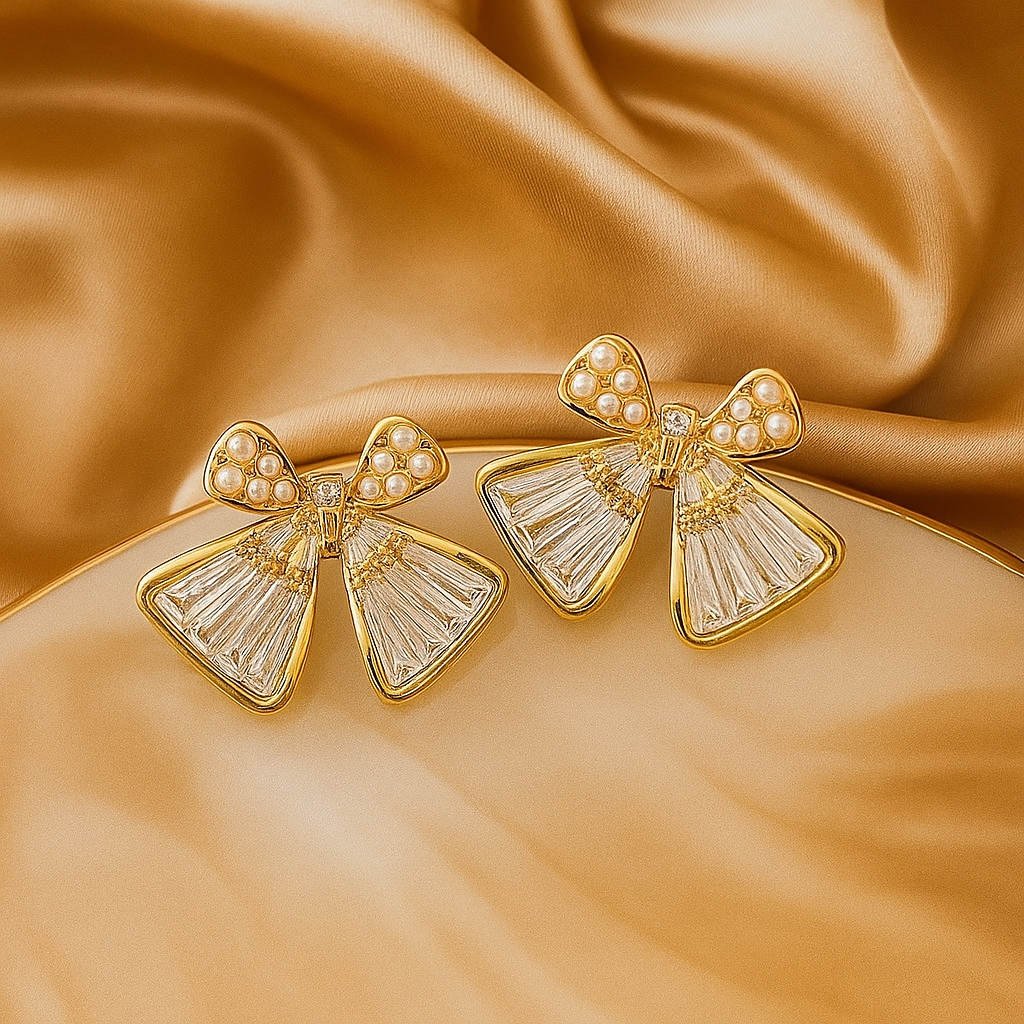Gold bow-shaped earrings with pearl centers on a satin background