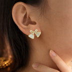 Gold bow-shaped earrings with clear stones worn by a person.