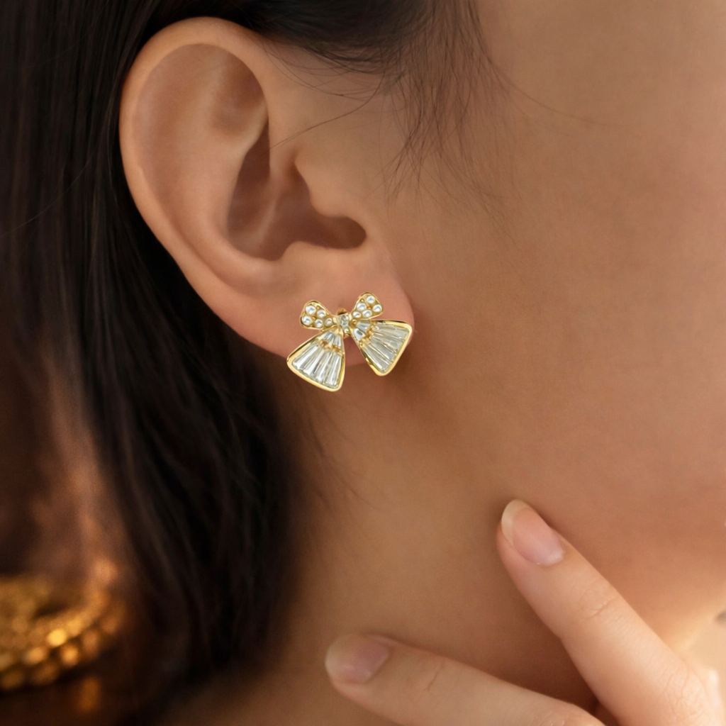 Gold bow-shaped earrings with clear stones worn by a person.