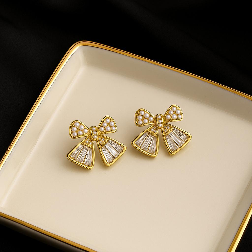 Gold bow-shaped earrings with pearl details on a beige tray.