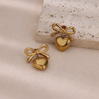 Gold heart-shaped earrings with bows on a textured surface