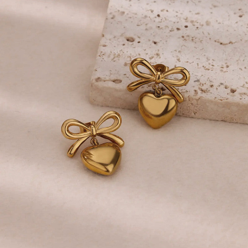 Gold heart-shaped earrings with bows on a textured surface