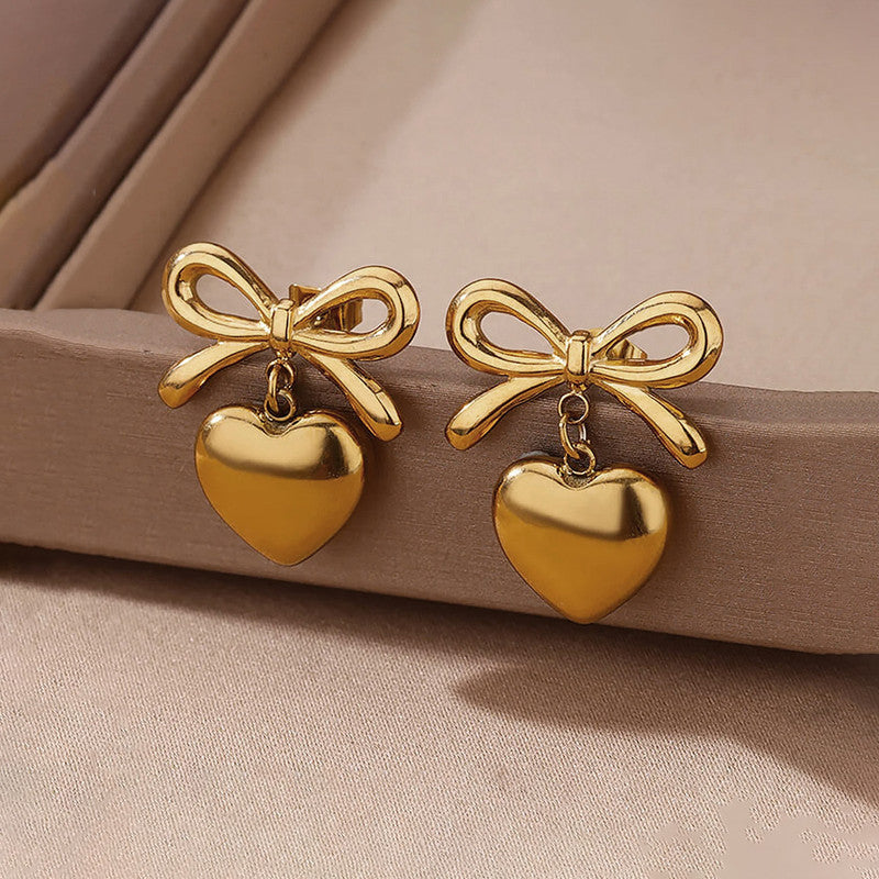 Gold bow and heart earrings on a beige surface