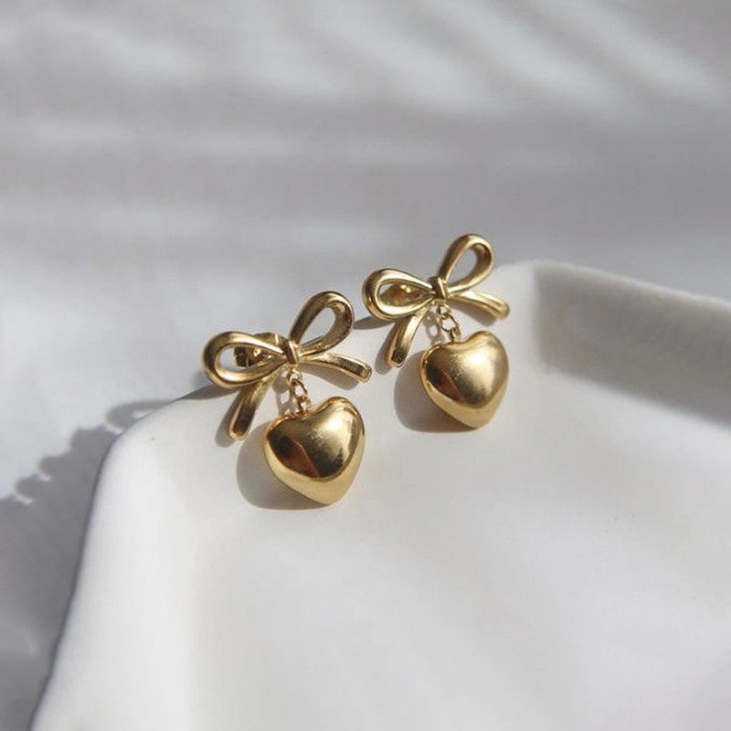 Gold bow and heart-shaped earrings on a white surface