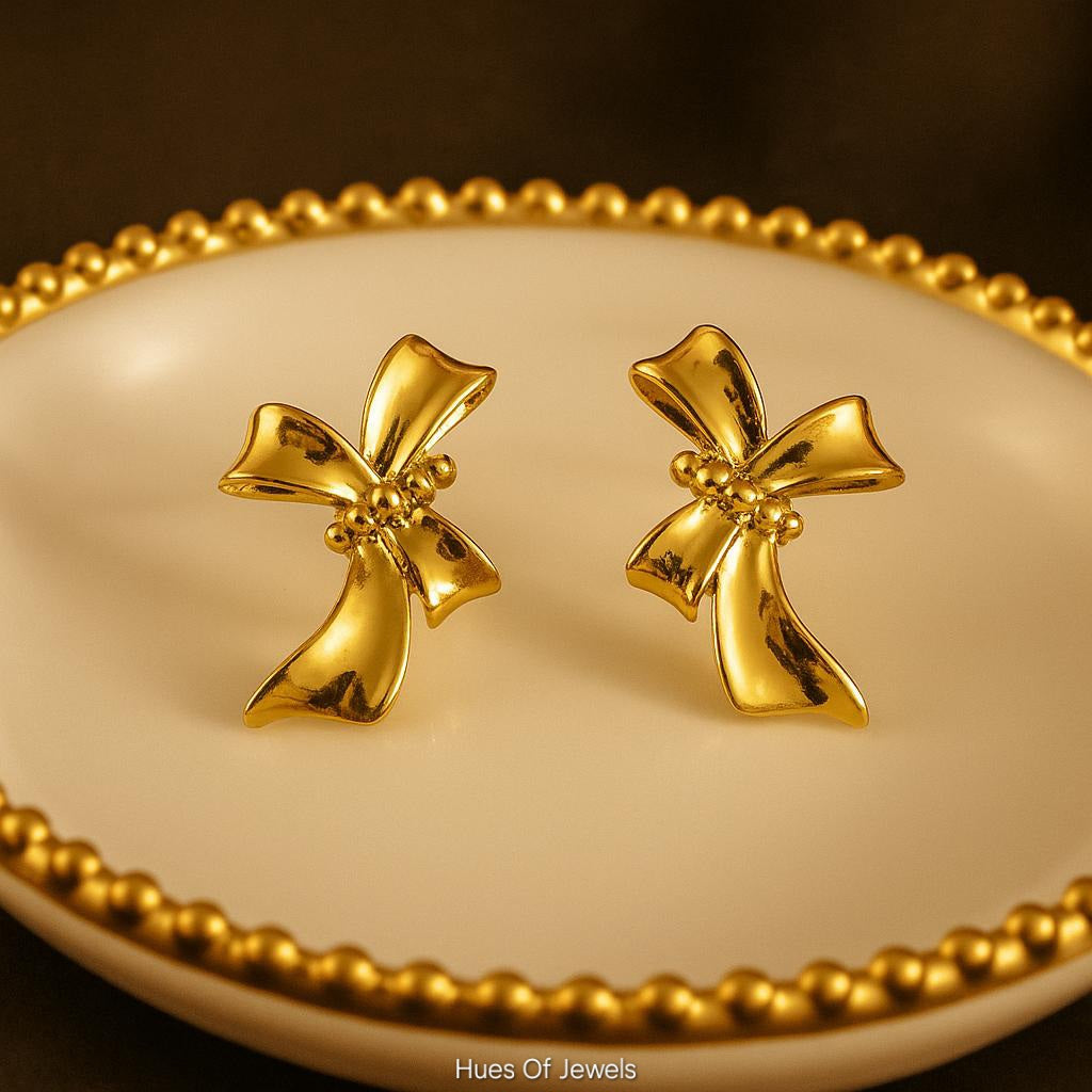 Gold bow-shaped earrings on a matching gold dish with a dark background.