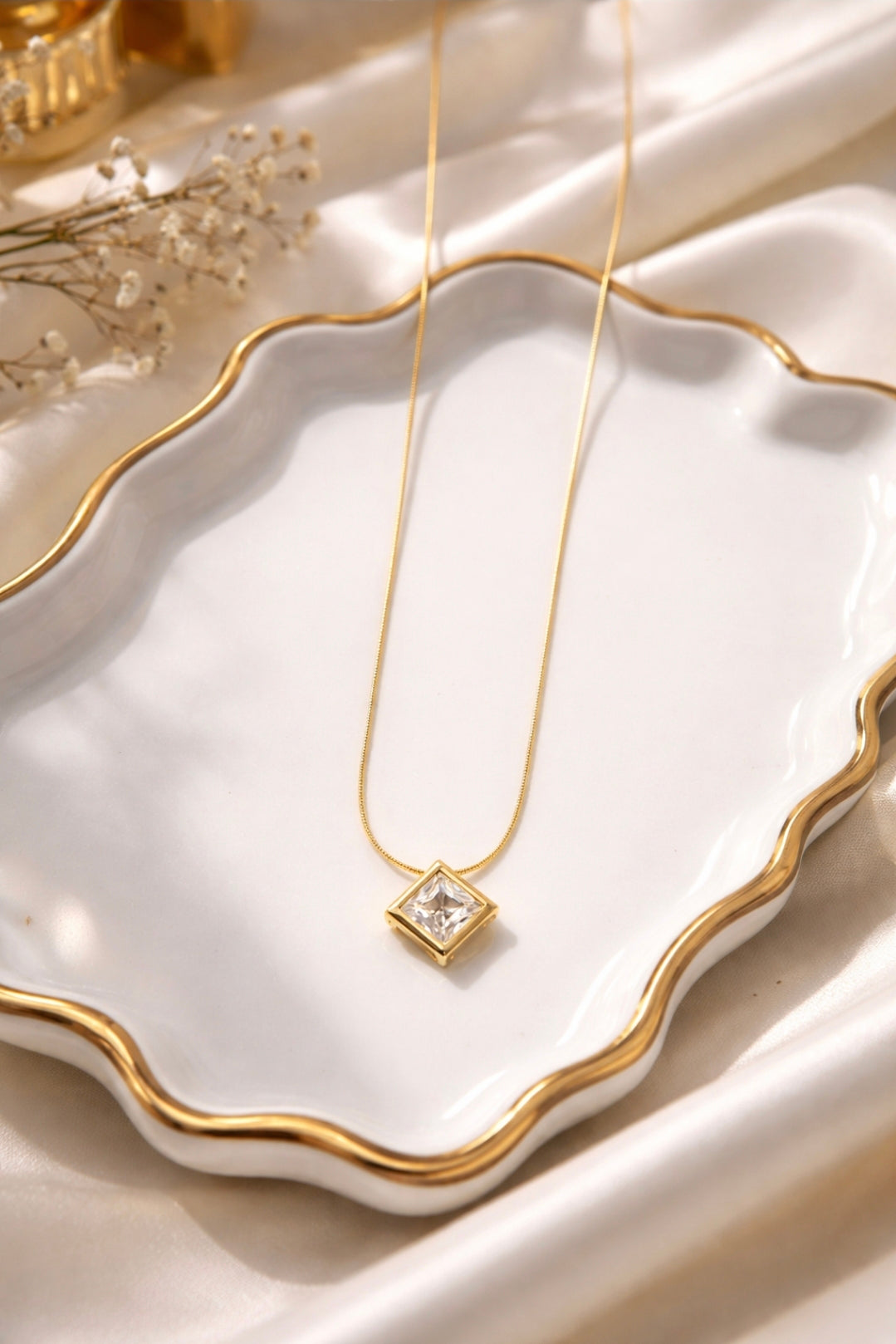 Gold necklace with a diamond pendant on a white dish with gold rim