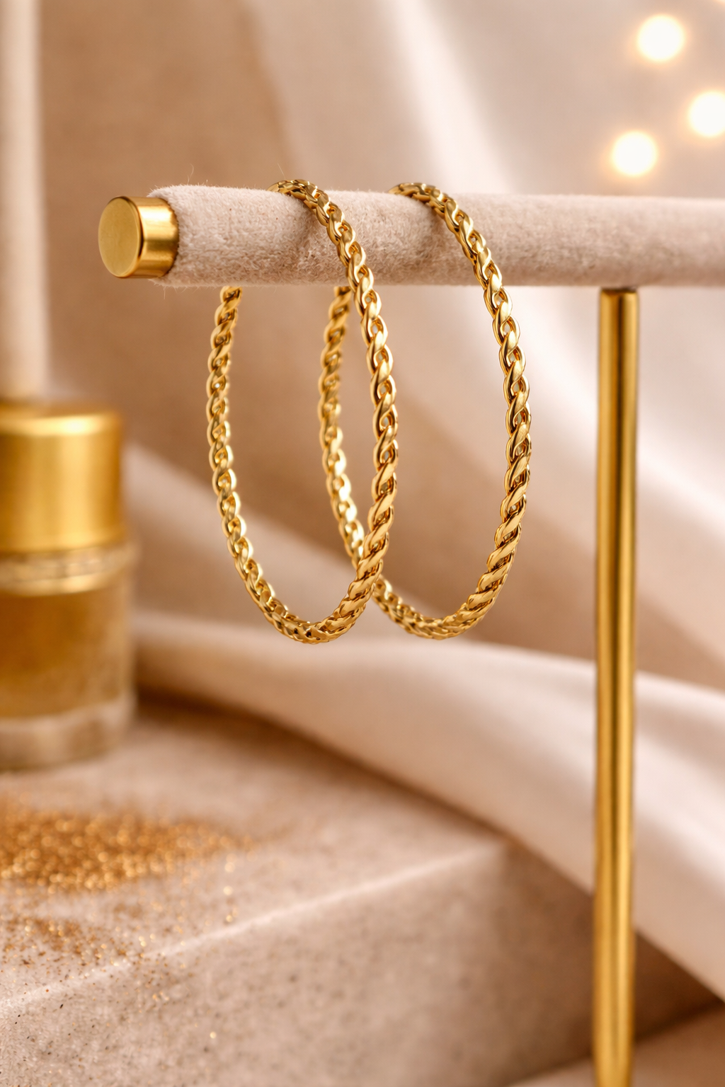 Two gold chain Bangles (Cirra Bangles) on a decorative stand with a soft, blurred background.