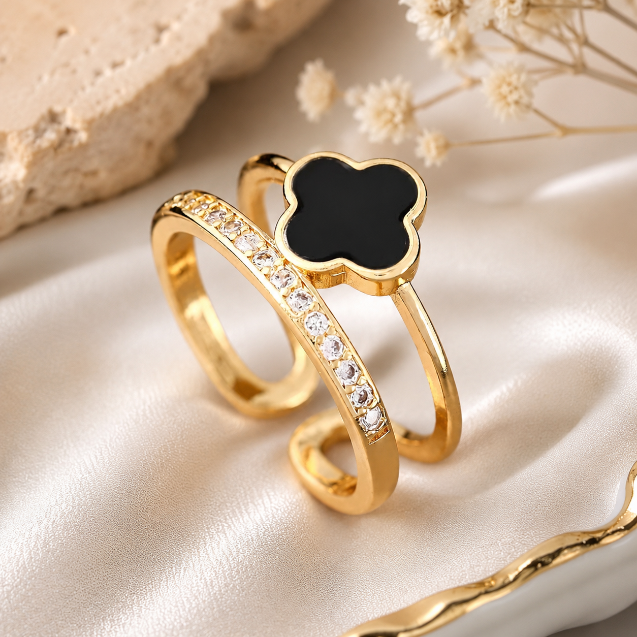 Gold ring with black clover-shaped center on a beige fabric background