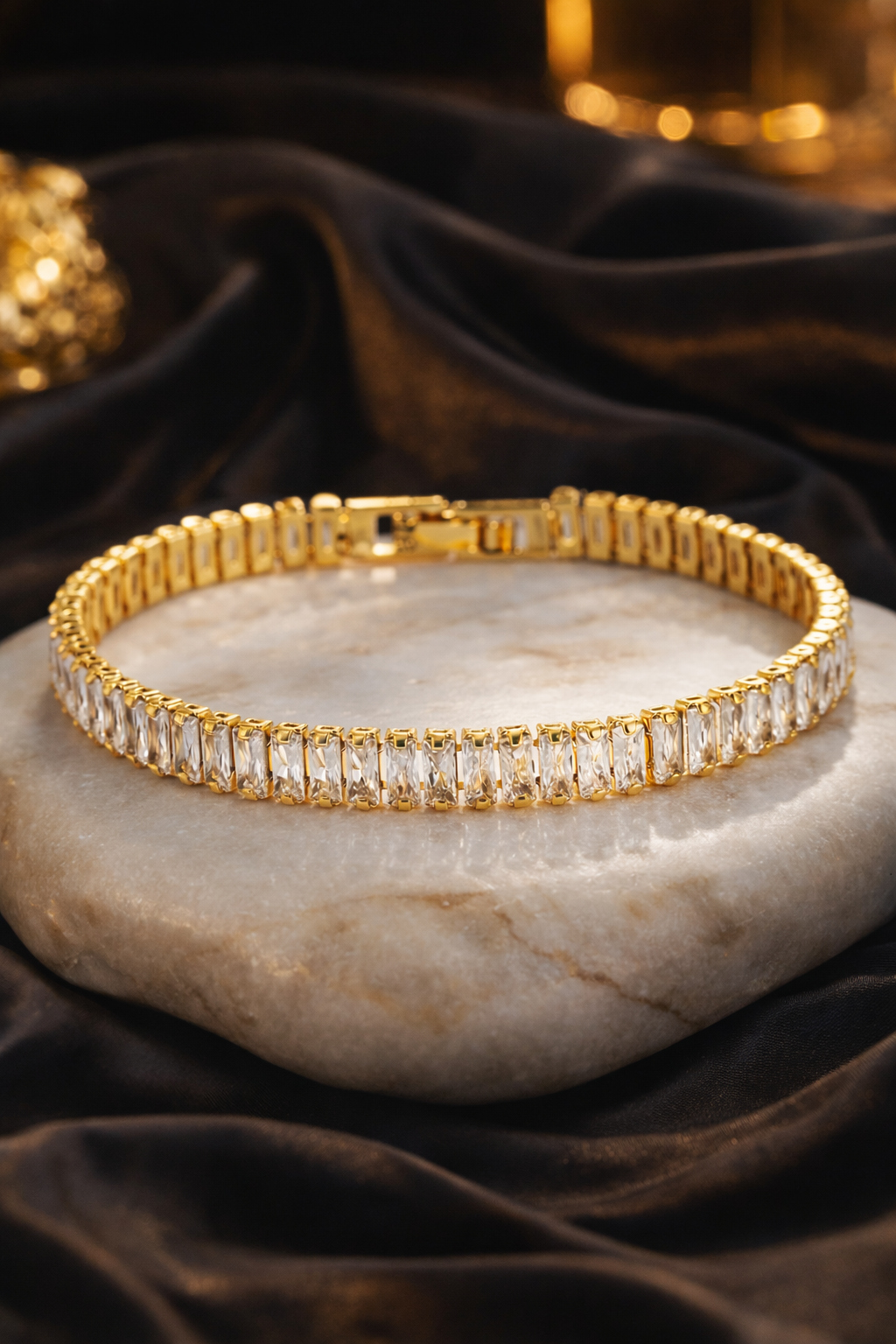 Gold tennis bracelet with clear stones on a marble surface with dark fabric background