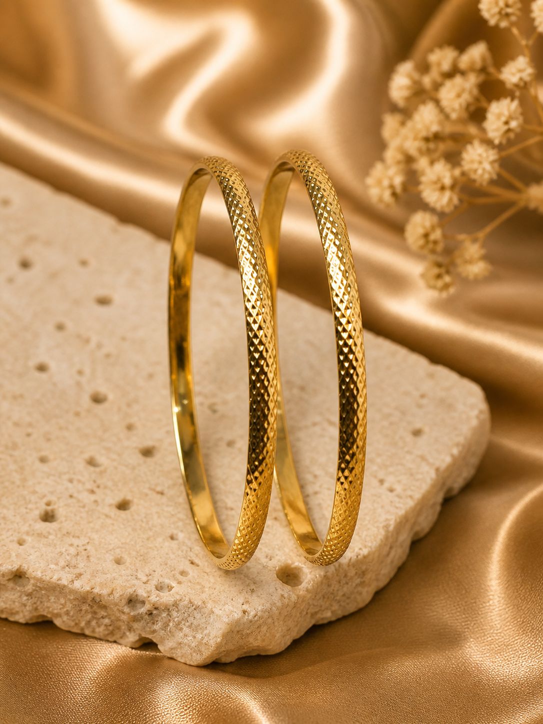 Anti tarnish golden bangles on a textured stone surface with a soft gold background
