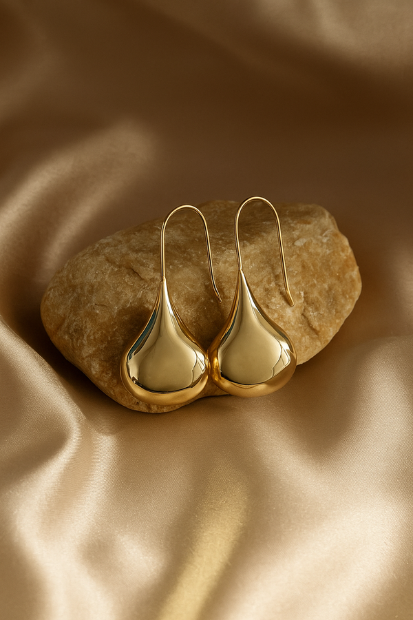 Gold teardrop earrings on a textured brown surface