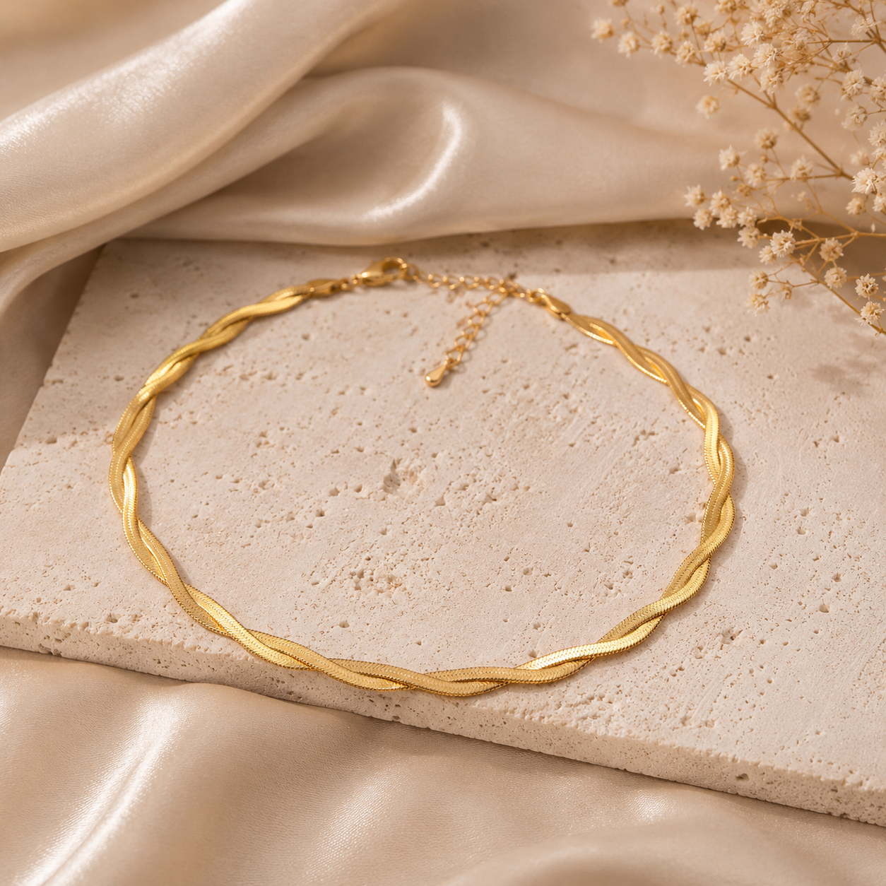 Gold necklace on a textured beige surface with dried flowers
