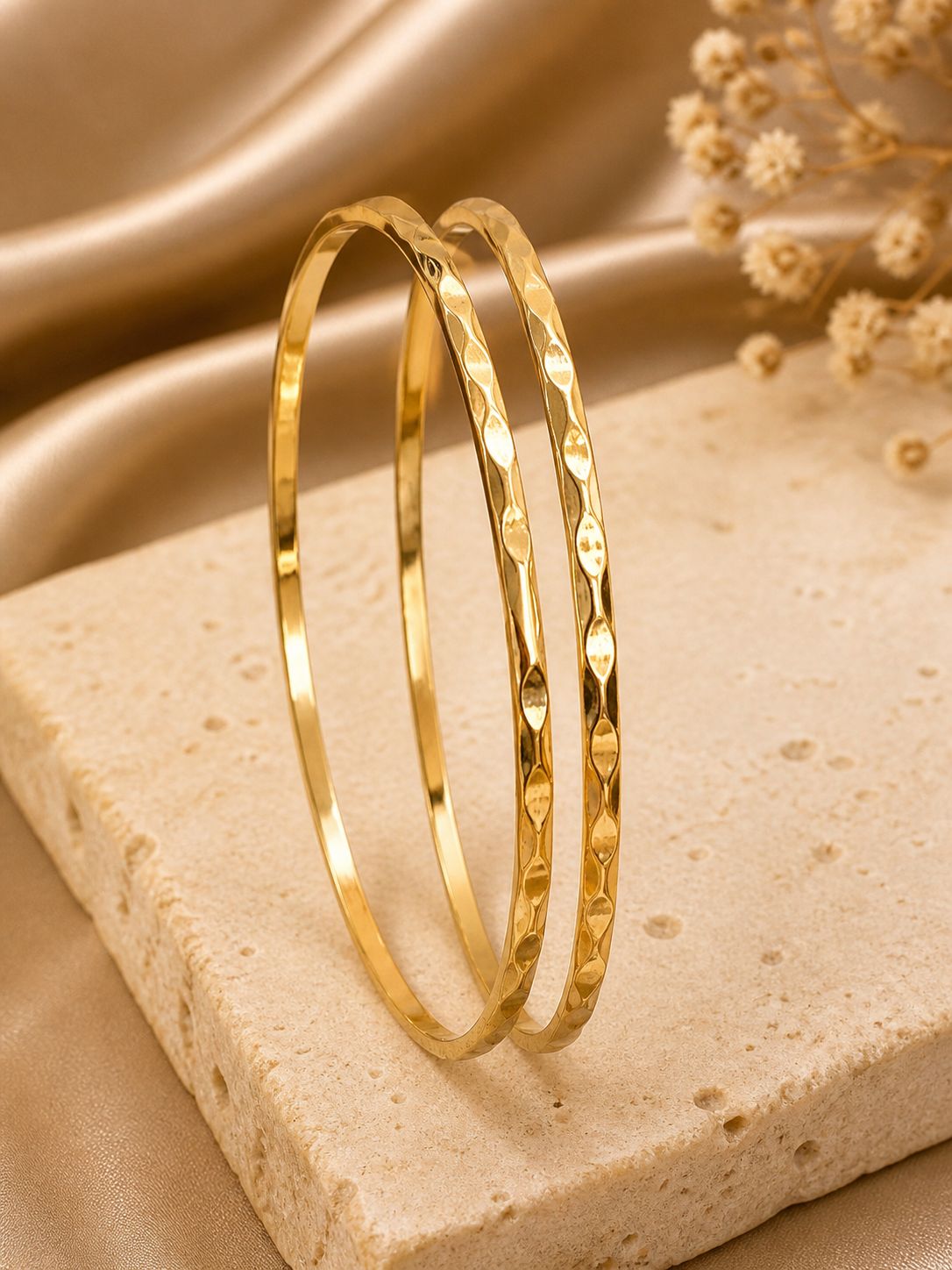 Two anti tarnish bangles on a beige stone surface with a soft beige fabric background.