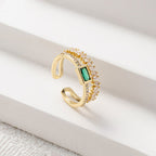 Gold ring with green gemstone and clear stones on a white surface