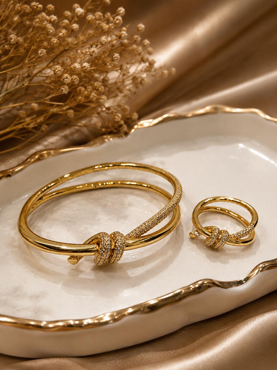 Golden anti tarnish bracelet and ring set on a decorative plate with dried flowers.