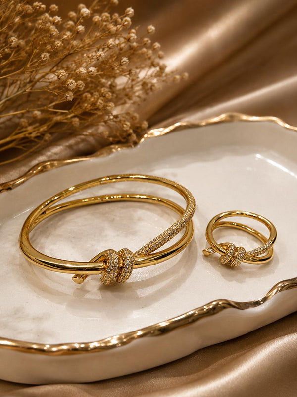 Golden anti tarnish bracelet and ring set on a decorative plate with dried flowers.