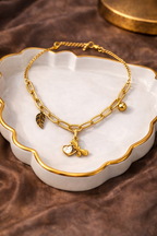 Gold neck chain with heart and leaf charms on a white dish with a brown background