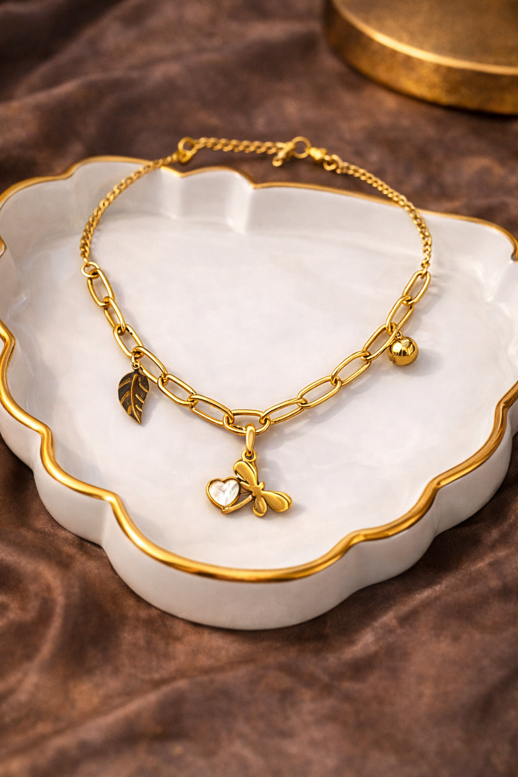 Gold neck chain with heart and leaf charms on a white dish with a brown background