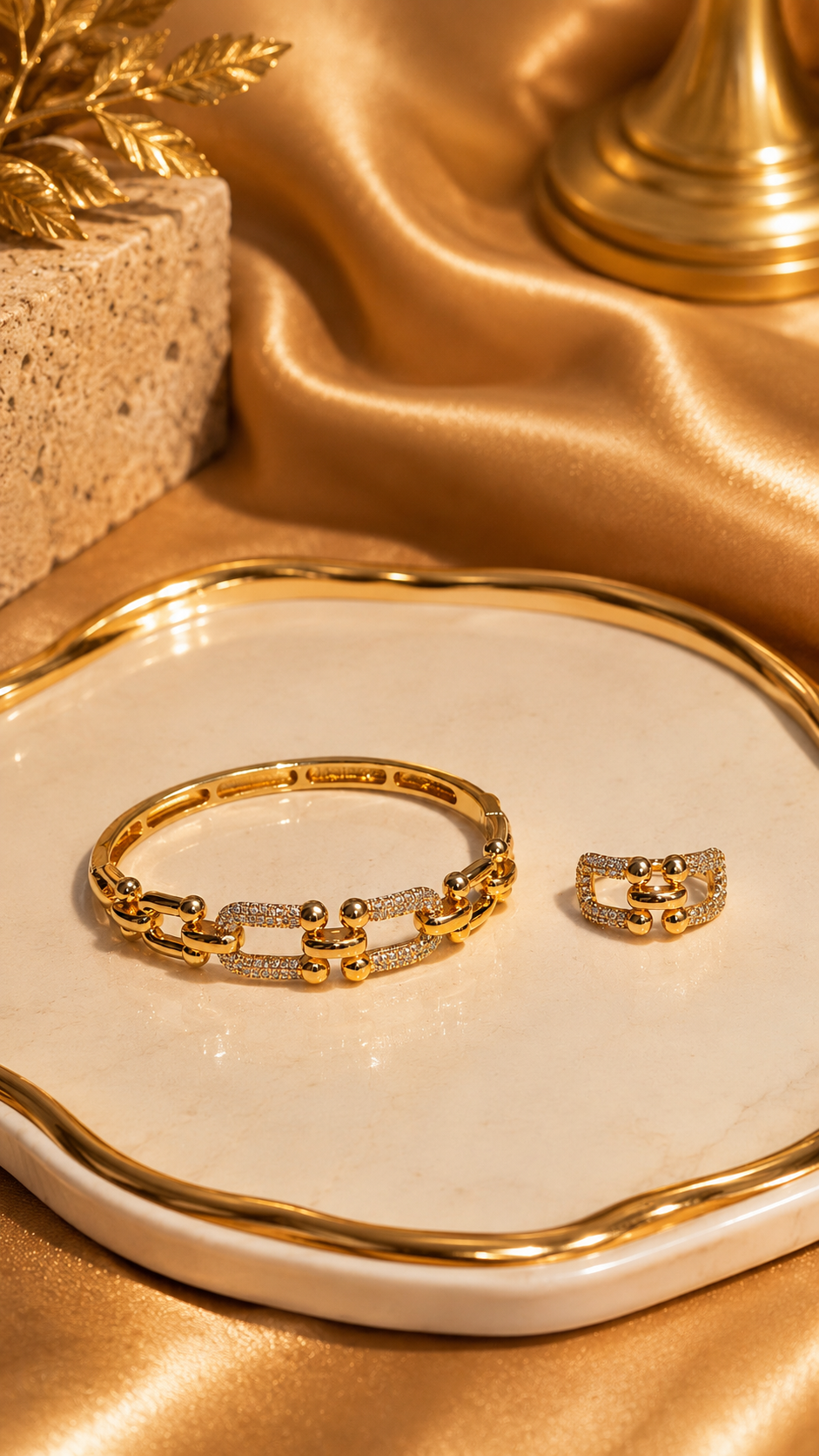 Gold bracelet and ring set on a white dish with gold fabric background