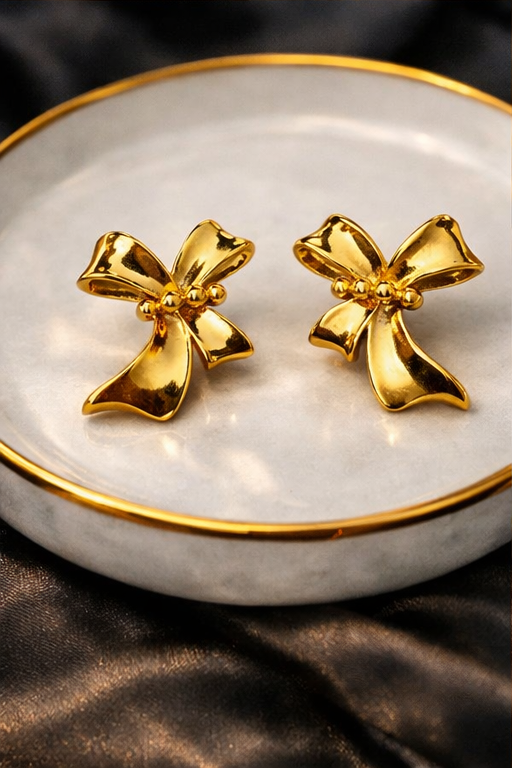 Gold bow-shaped earrings on a white dish with gold rim