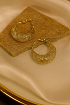 Pair of gold hoop earrings on a beige fabric background