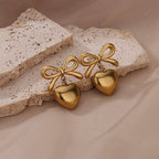 Gold bow and heart-shaped earrings on a textured beige surface