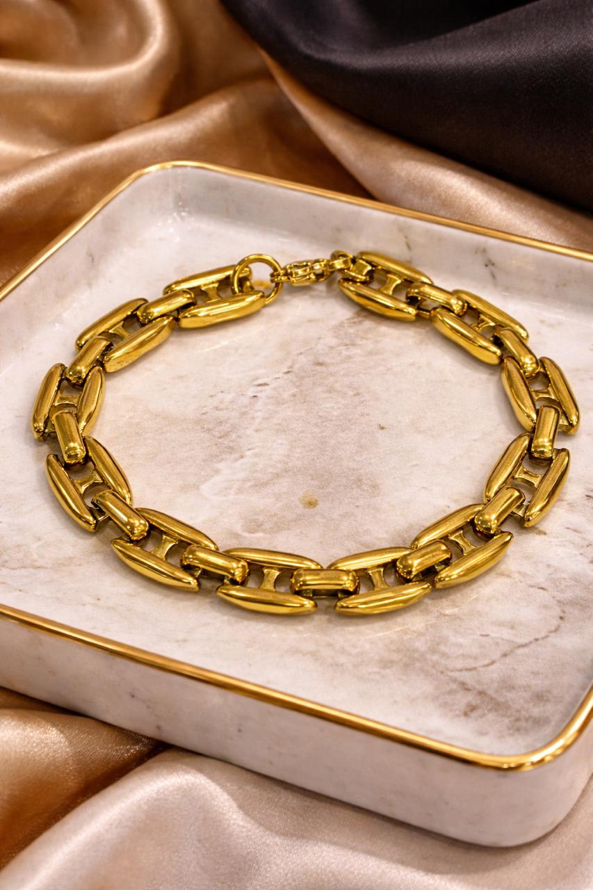 Gold chain bracelet on a marble surface with a soft fabric background