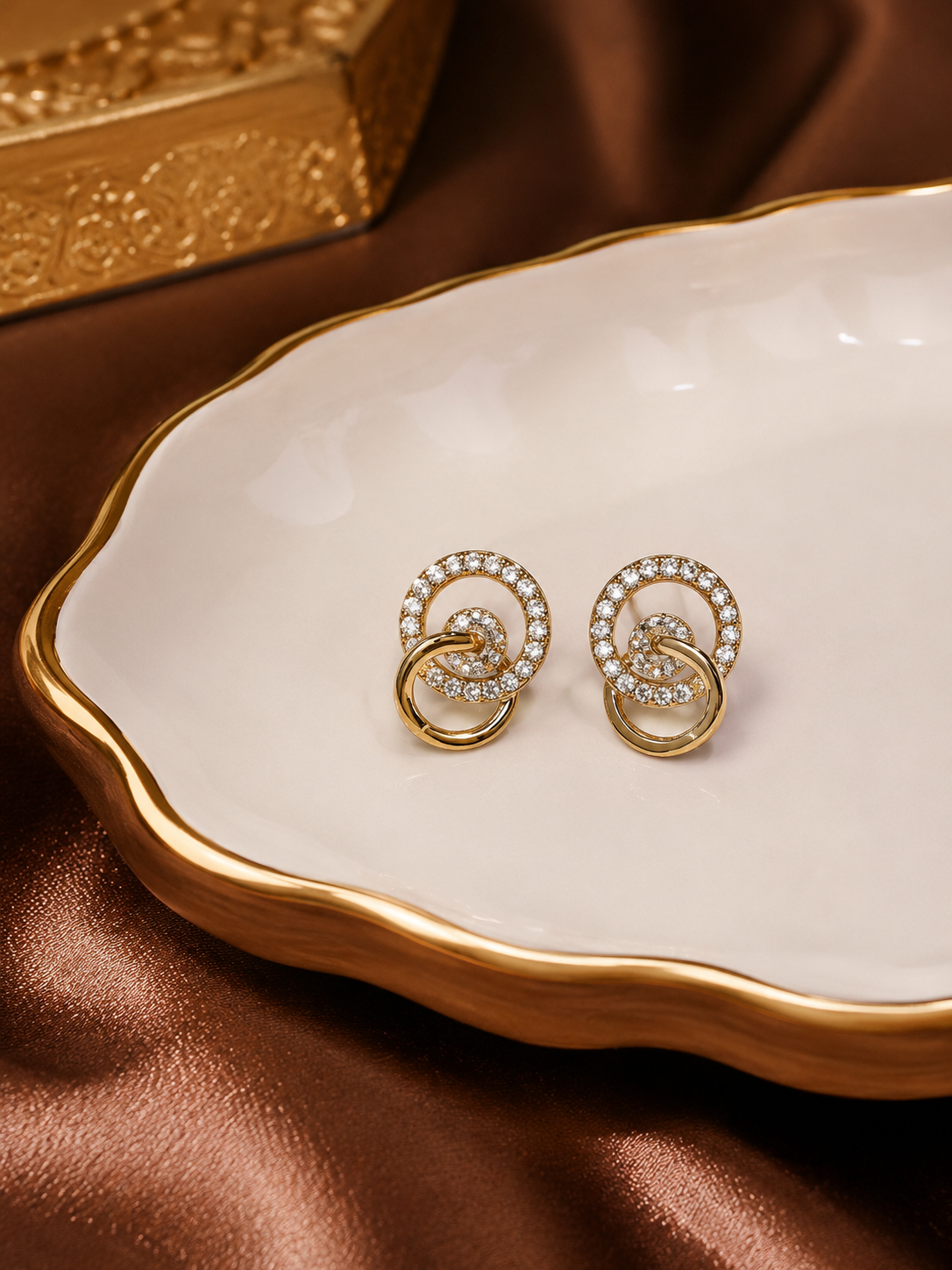 Anti tarnish earrings with circular design on a white dish with gold rim against a brown fabric background