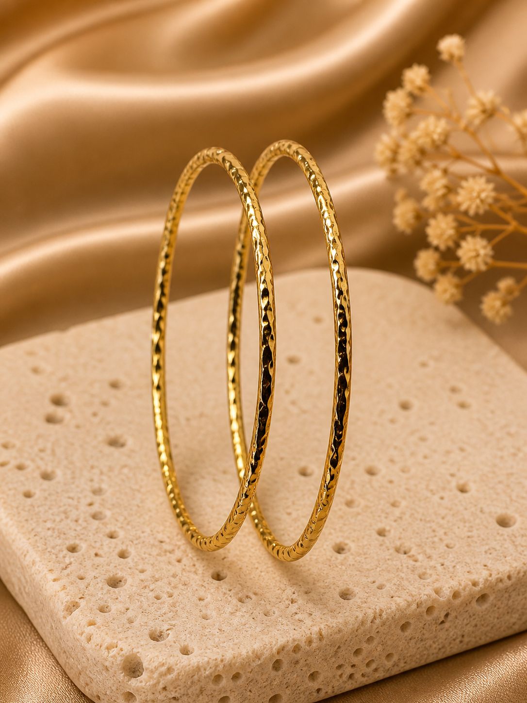 Two anti tarnish golden bangles on a textured beige surface with a soft brown background