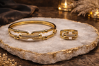 Gold bracelet and ring on a decorative stone surface with warm lighting