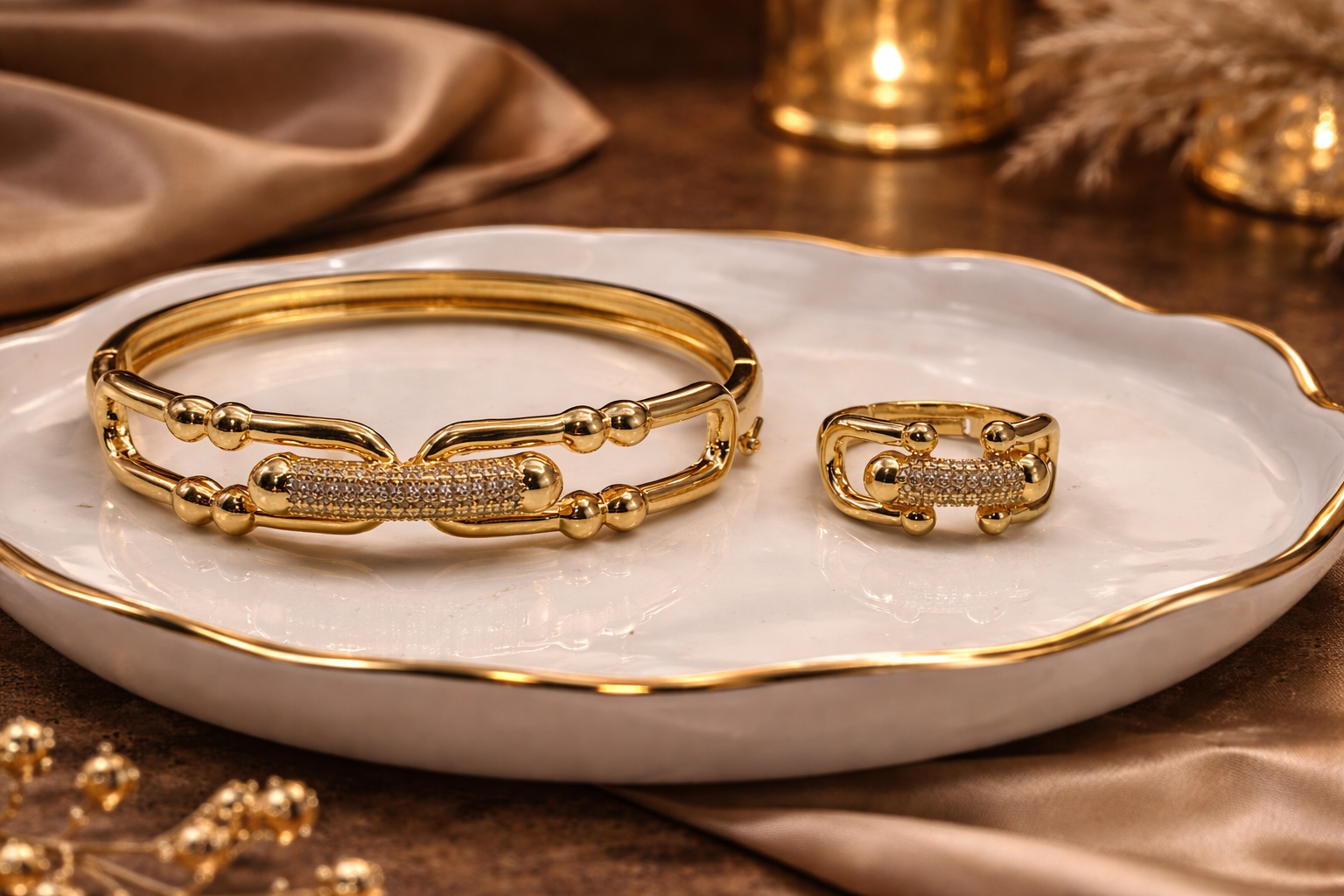 Gold bracelet and ring set on a white dish with a warm background