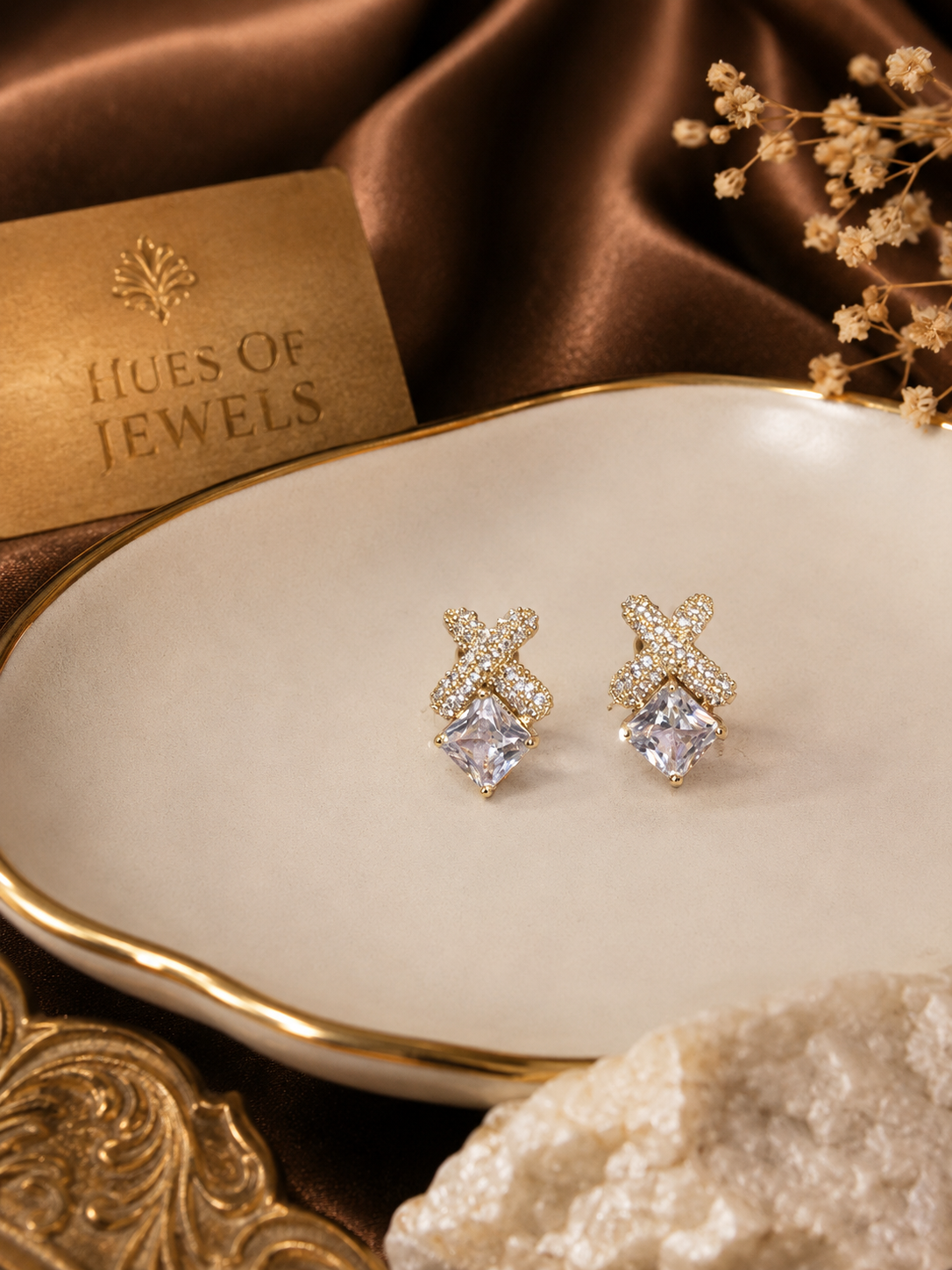 Anti tarnish nexa earrings with clear stones on a white dish, with 'Hues of Jewels' card in the background.
