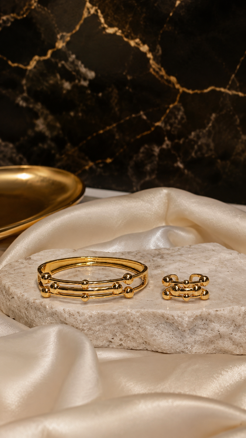 Gold bracelet and ring on a marble surface with a dark marble background