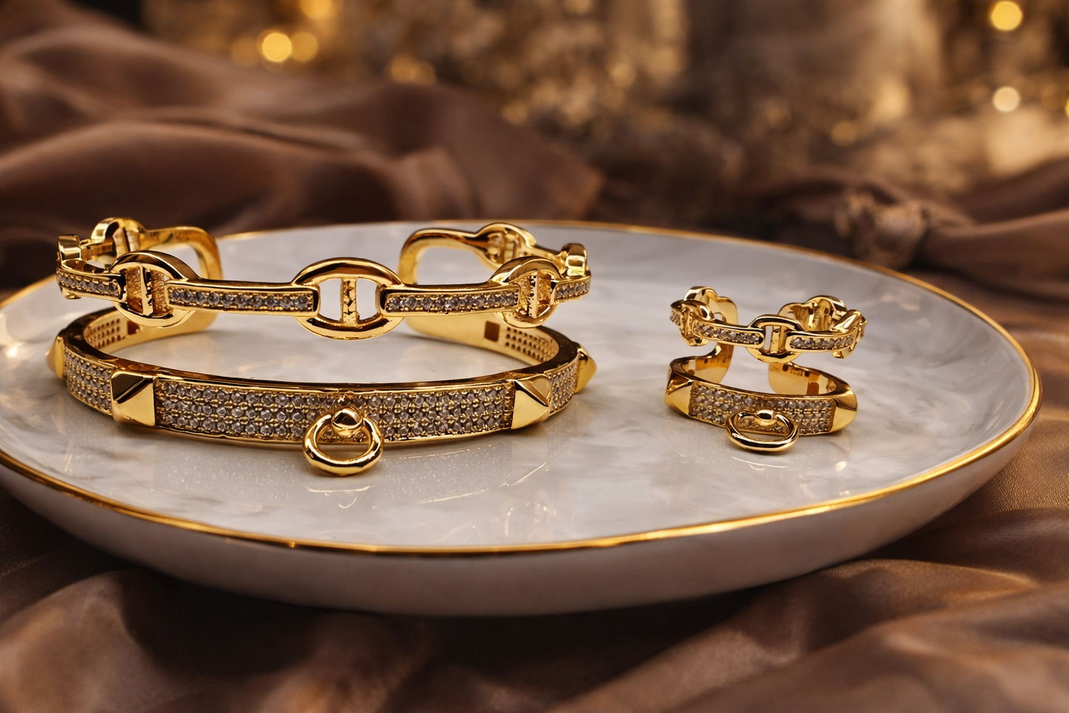 Gold jewelry set including bracelets and earrings on a marble plate with a brown fabric background.