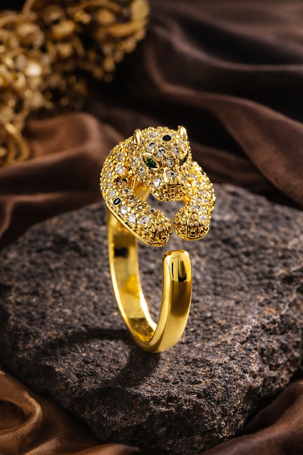 Gold panther-shaped ring on a dark stone surface with brown fabric background