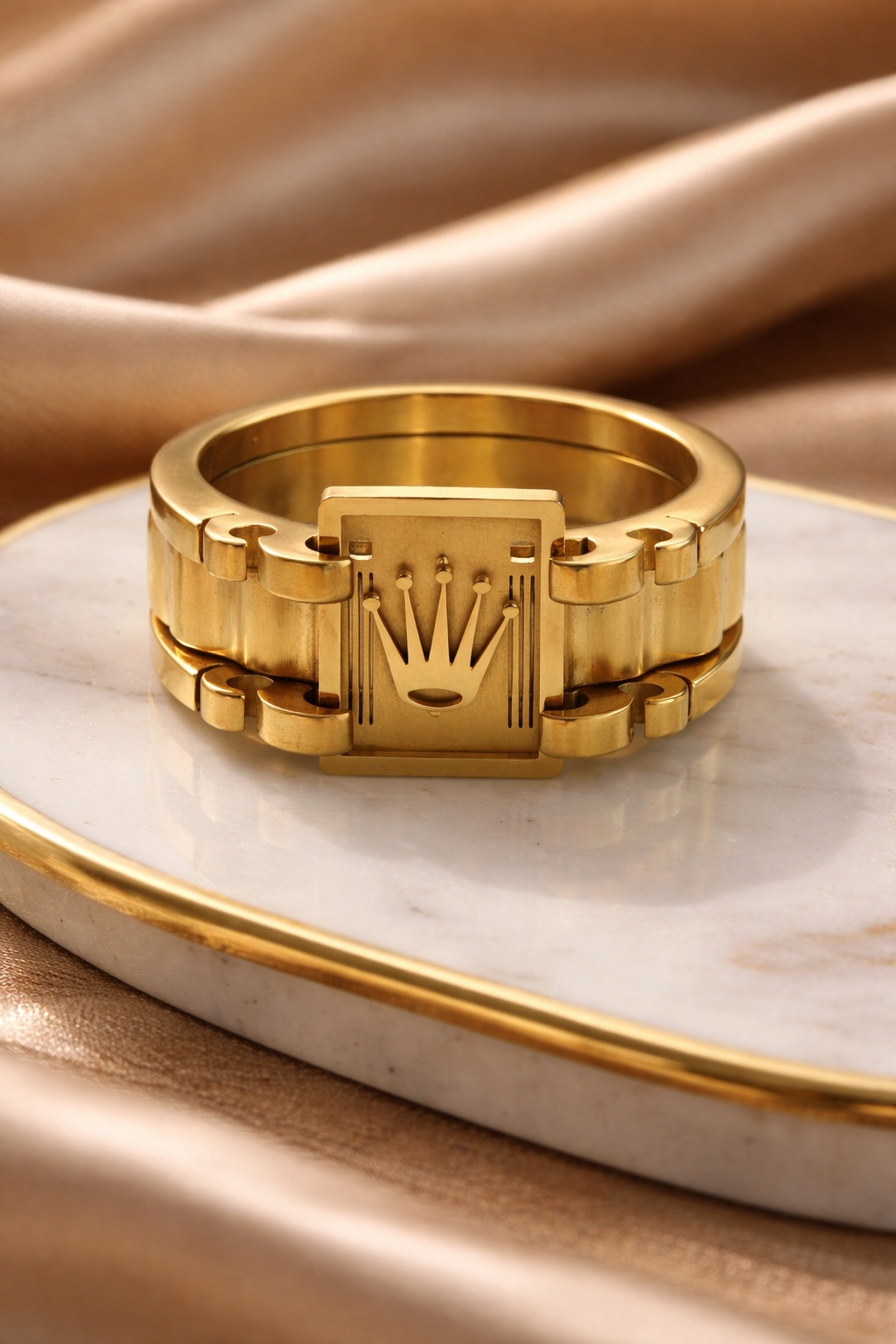 Gold ring with a prominent crown design on a marble surface