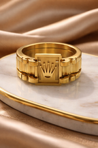 Gold ring with a prominent crown design on a marble surface