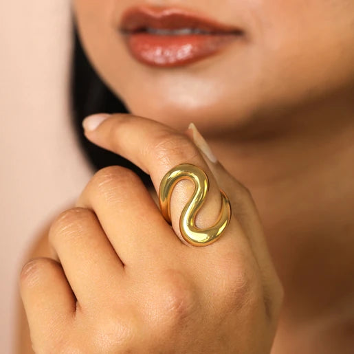 S shaped Gold ring on a finger with a blurred background