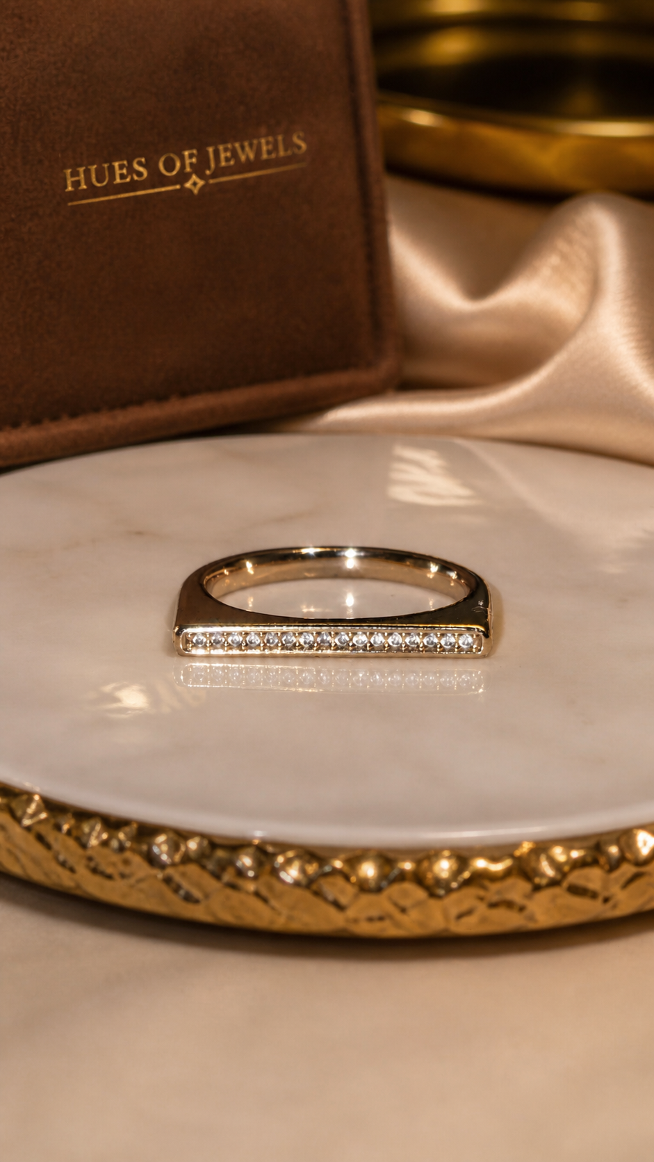 Gold ring on a white dish with 'Hues of Jewels' branding in the background