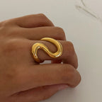 Sway Gold ring on a person's finger against a neutral background