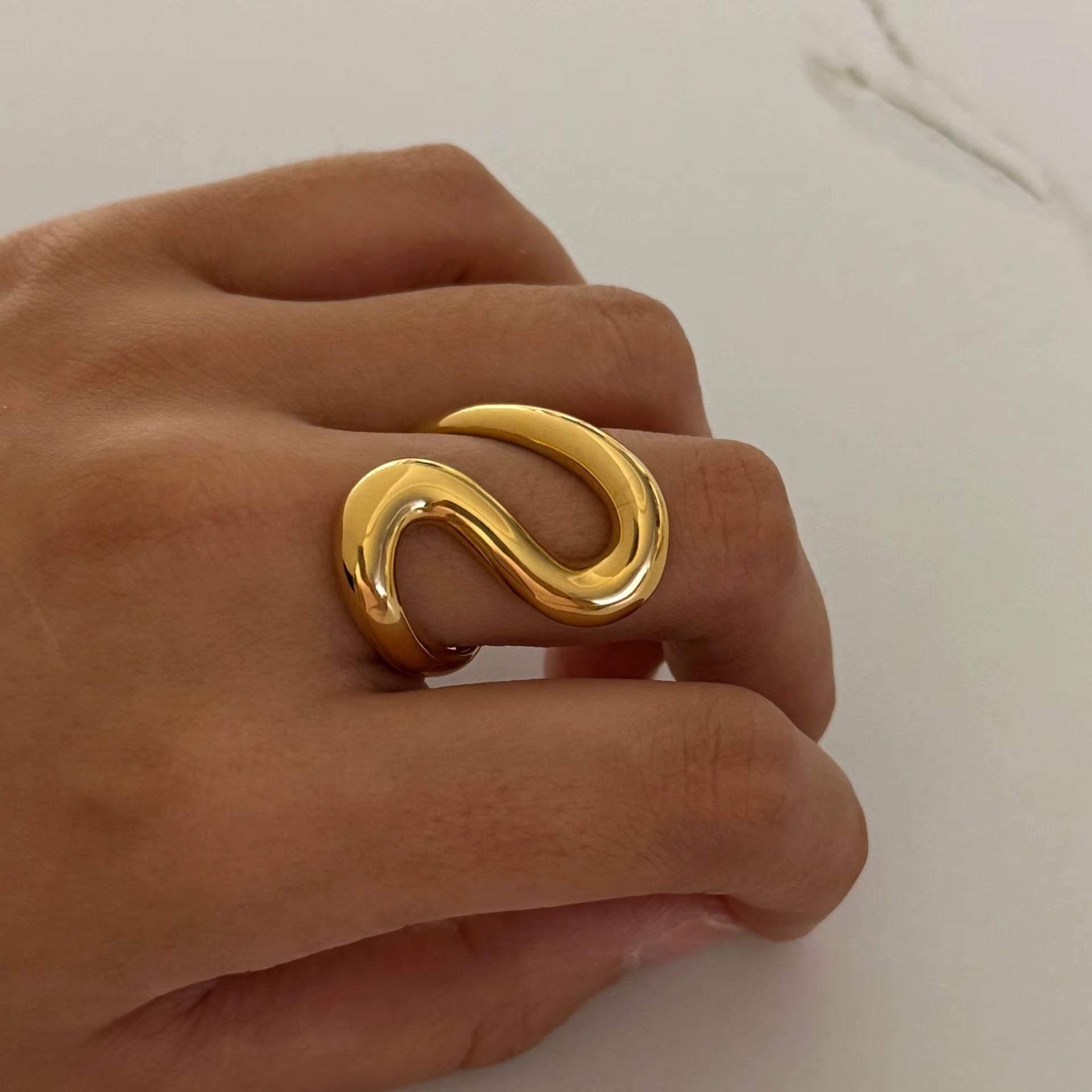 Sway Gold ring on a person's finger against a neutral background
