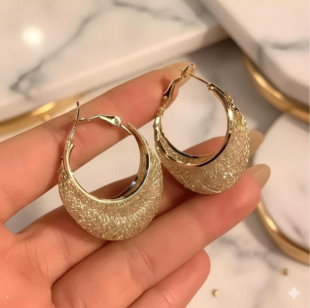 Gold hoop earrings held in a hand with a marble background