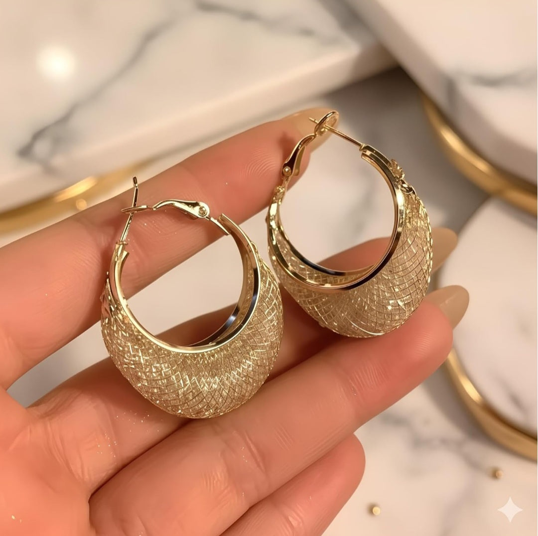 Gold hoop earrings held in a hand with a marble background