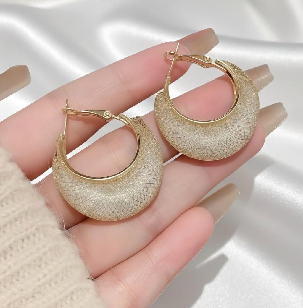 Gold hoop earrings held in a hand against a neutral background