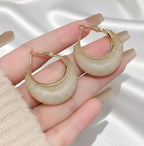 Gold hoop earrings held in a hand against a neutral background