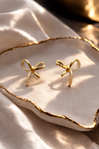 Gold bow-shaped earrings on a beige surface with a gold rim
