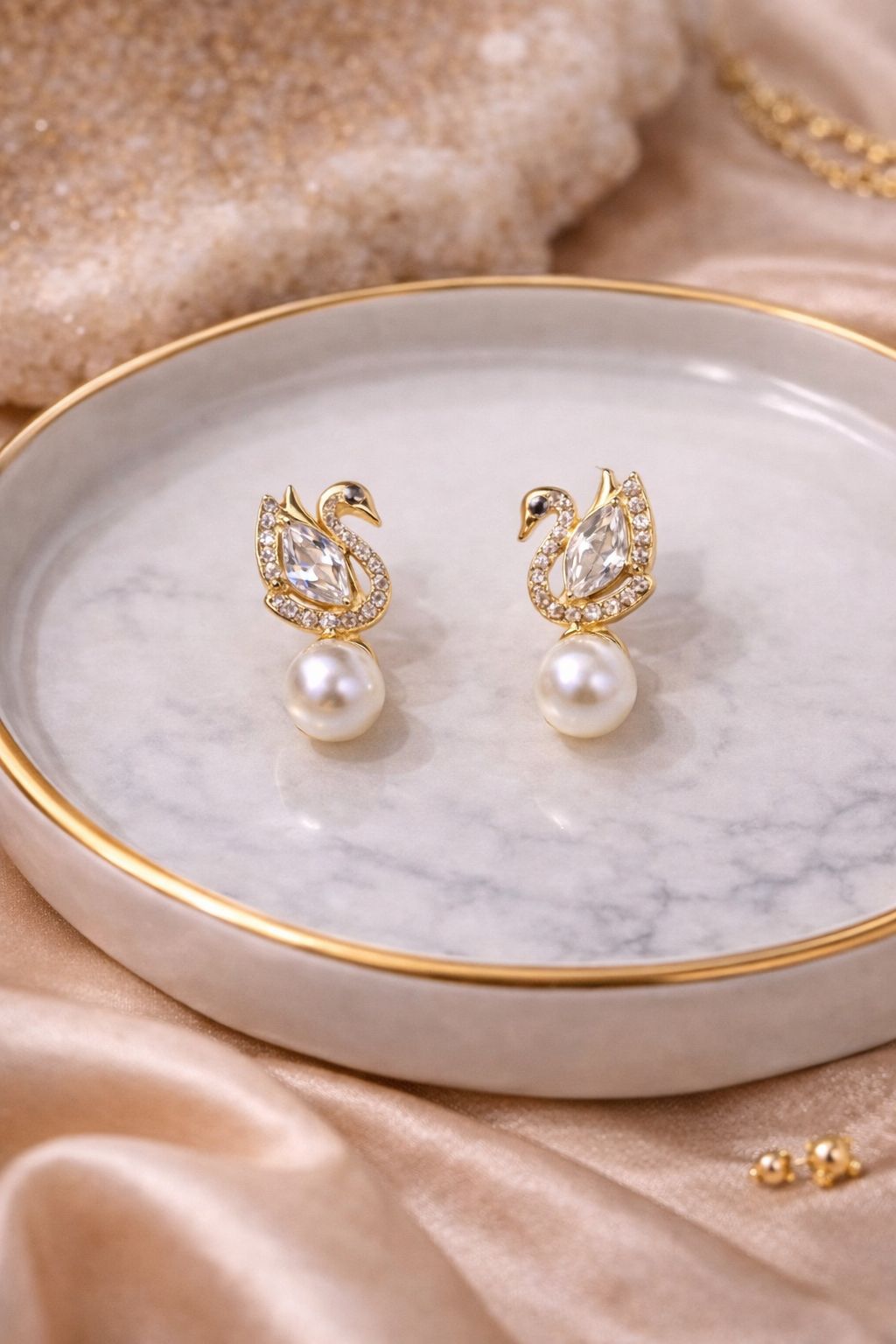 Anti tarnish swan shaped studded pearl earrings on a marble dish with a soft fabric background