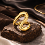 Gold spiral ring on a textured stone surface with a brown fabric background