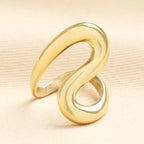 Gold ring with a wavy design on a beige background