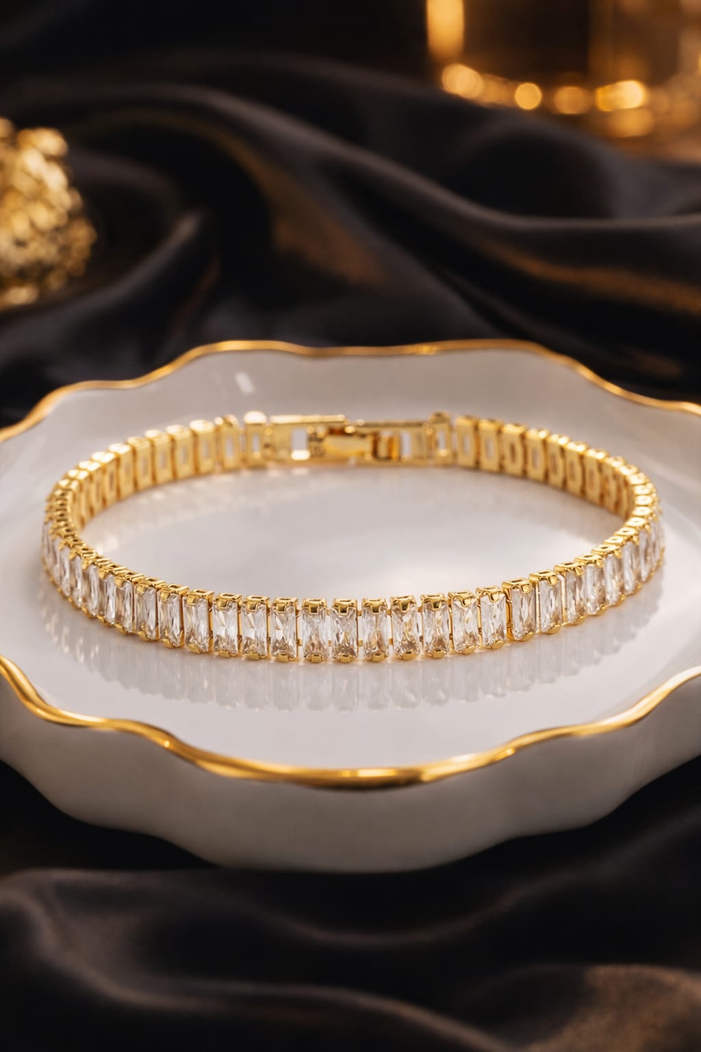 Gold bracelet with clear stones on a white dish with gold rim against a dark fabric background